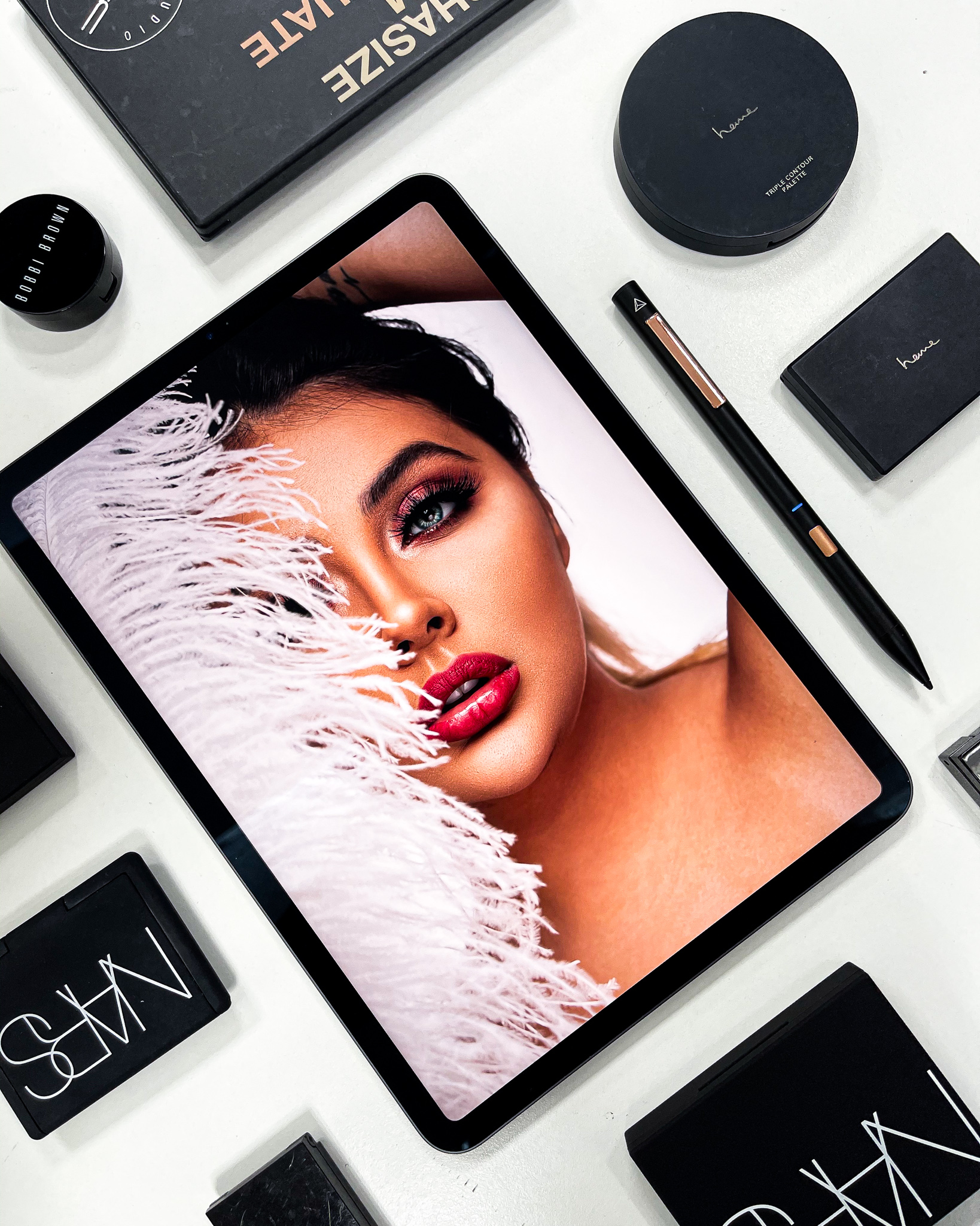 Beauty portrait retouched on iPad, surrounded by makeup palettes