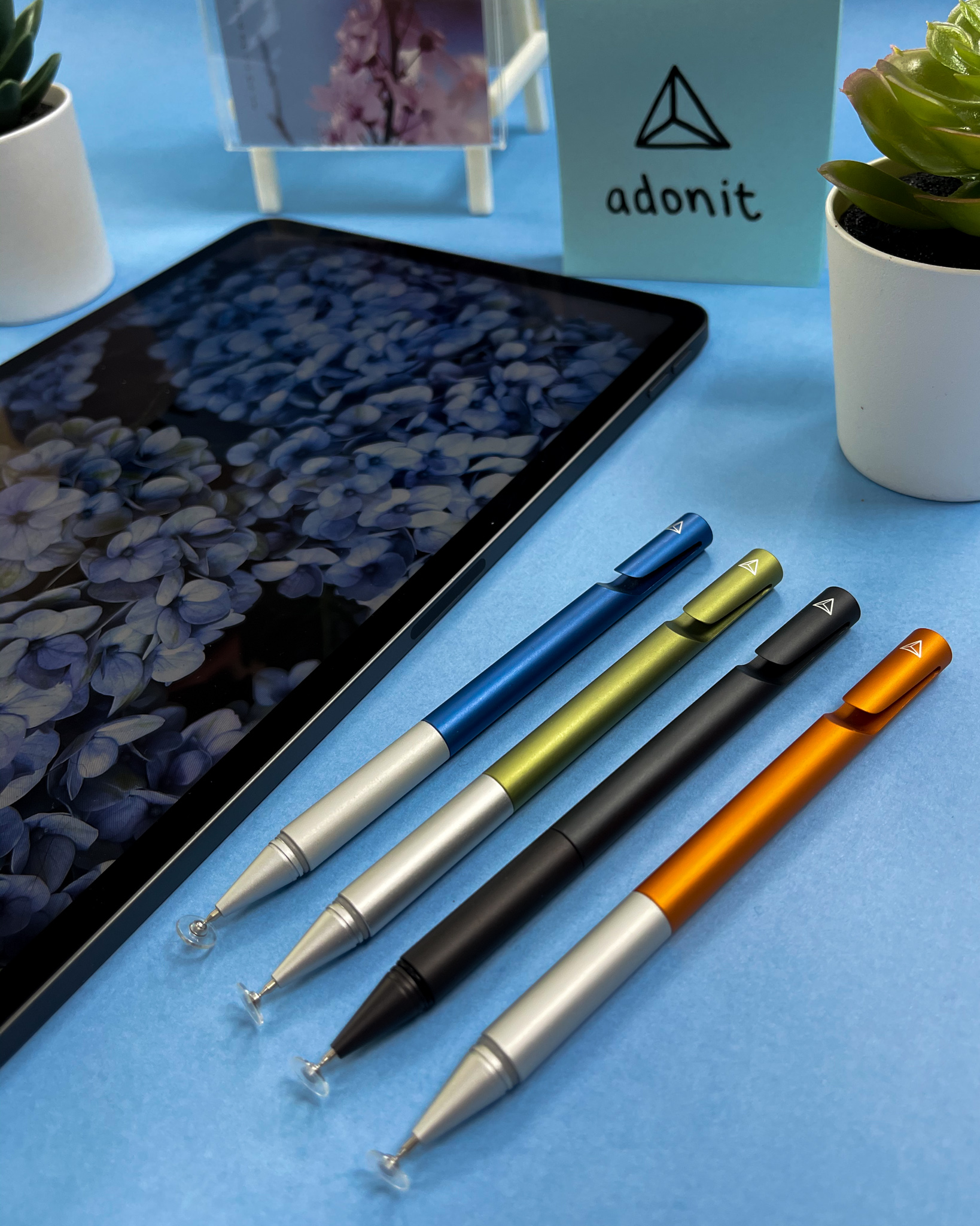 Four coloured Adonit pens lined up on a blue desk
